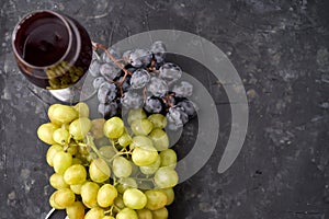 Bunches of ripe green and blue grapes with a glass of red wine, a corkscrew and wine corks on a dark stone background. Top view.