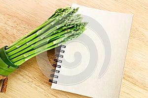 Bundle of asparagus on wooden background and blank diary b