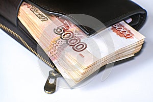 A bundle of banknotes in a leather wallet. Next to it is a stack of hundred-dollar bills