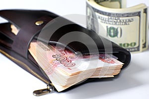 A bundle of banknotes in a leather wallet. Next to it is a stack of hundred-dollar bills