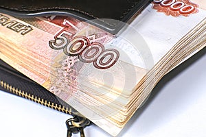 A bundle of banknotes in a leather wallet. Next to it is a stack of hundred-dollar bills