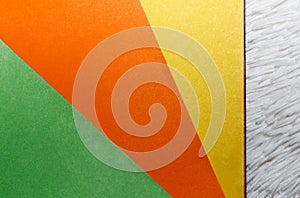 A bundle of colored paper lies on a white background. Three-color geometric surface, orange, yellow and green