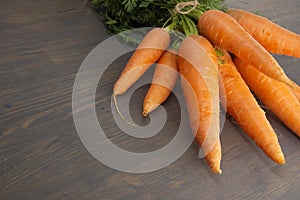 Bundle of fresh, orange carrots with green tops on wooden table