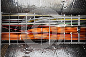 Bundle of orange ethernet cables routed in a building ceiling along the ventilation system. Bottom-angle view, no people photo
