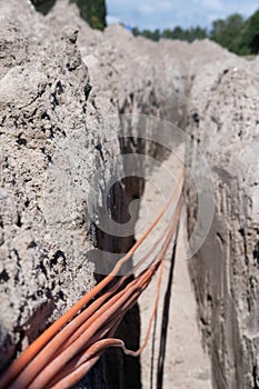 Bundle of orange fiber optic cables lie in a dug trench in the ground in a street