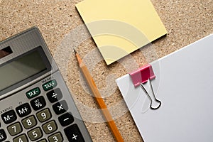 A bundle of paper sheets with a clip, a calculator and a pencil on a chipboard table