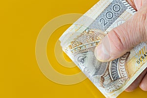 A bundle of Polish money, Two hundred zloty banknotes, Held in hands. Yellow background with place for text