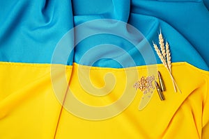 Bundle of wheat spikes and live ammunition on Ukrainian flag background, Concept of food supply crisis and global food scarcity