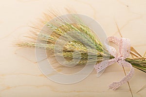 A bundle of wheat on a wooden board tied with a pink lace ribbo