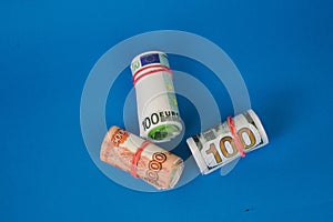 bundles of twisted money of different currencies on a blue background