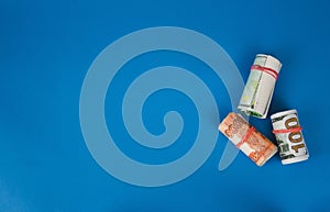 bundles of twisted money of different currencies on a blue background