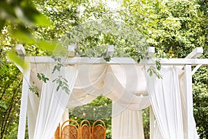 Bungalow with roof with light curtains in garden. Summer gazebo with flowing white curtains for relax outdoor.