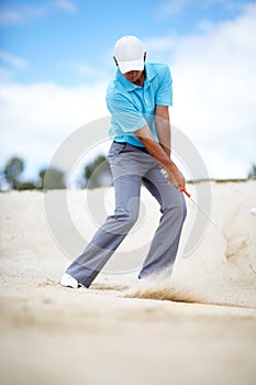 In the bunker. An image of a young male golfer chipping his ball out of a bunker in a game of golf.