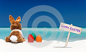 Bunny, easter eggs and Happy Easter sign on a beach