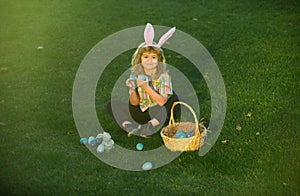 Bunny kids with rabbit bunny ears. Easter egg hunt in garden. Child boy playing in field, hunting easter eggs.