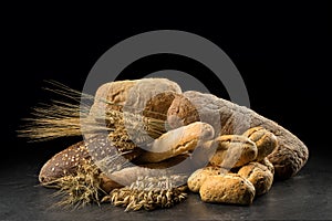 Buns, baguette, ciabatta and bread on dark wooden table. Rye, barley, wheat, oats and many fresh mixed breads on black ba