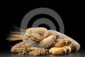 Buns, baguette, ciabatta and bread on dark wooden table. Rye, barley, wheat, oats and many fresh mixed breads on black ba