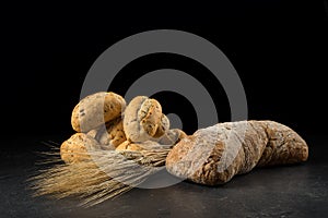 Buns and ciabatta, bread on dark wooden table. Barley and fresh mixed breads isolated on black background