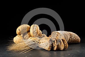 Buns and ciabatta, bread slices on dark wooden table. Barley and fresh mixed breads on black background