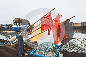 Buoy flag makers on poles above rope and fishing next baskets in Whitstable harbour. Fisherman huts and fishing boats can be seen