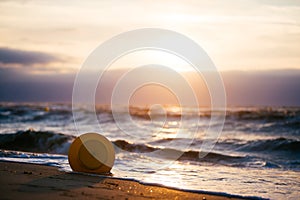 A buoy by the sea in back-light with a cloudy sky and a setting sun