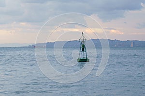 A buoy in the sea, in the background cargo ships and the coast.