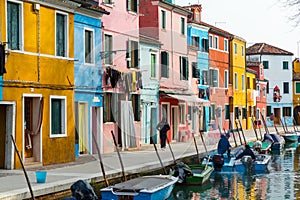 Burano island with colorful houses and buildings on embankment of narrow water canal with fishing boats
