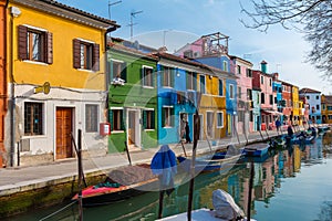 Burano island with colorful houses and buildings on embankment of narrow water canal with fishing boats