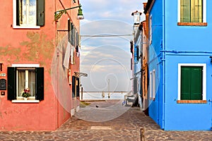 Burano island picturesque street and courtyard with small colorful houses in row against cloudy blue sky and Adriatic