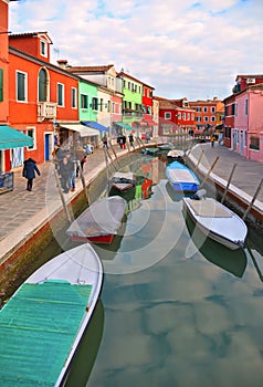 Burano island picturesque street with small colored houses in row, water canal with fishermans boats, cloudy blue sky