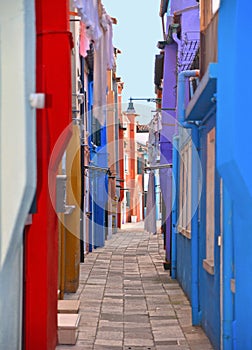 Burano island picturesque very narrow street and courtyard with small colorful houses in row against cloudy blue sky, Venice Italy