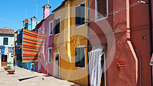 Burano, Venice, Italy. Street with colorful houses and colored tablecloth spread out to dry