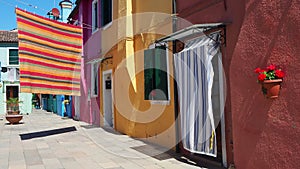 Burano, Venice, Italy. Street with colorful houses and colored tablecloth spread out to dry