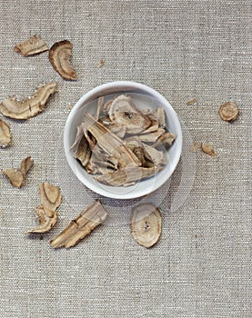 Burdock herb dried roots in a bowl flat from above on linen textile, overhead top view of wheat-grass