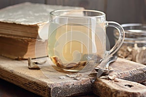 Burdock root tea in a glass cup with dry herb and old apothecary books nearby on wooden rustic background