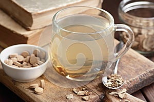 Burdock root tea in a glass cup with dry herb and old apothecary books nearby on wooden rustic background,