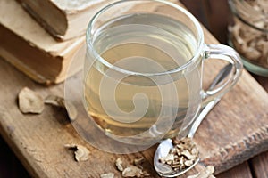 Burdock root tea in a glass cup with dry herb and old apothecary books nearby on wooden rustic background,