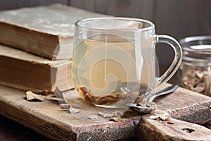Burdock root tea in a glass cup with dry herb and old apothecary books nearby on wooden rustic background