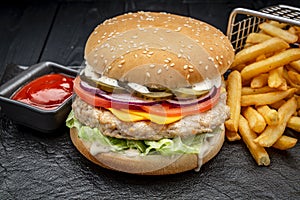 Burger with chicken cutlet and french fries on a dark background