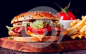 Burger with chicken cutlet, fried bacon and vegetables, French fries, glass of beer, on a wooden board, no people