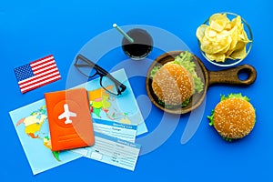 Burger, chips, map, passport, tickets and usa flag for gastronomical tourism to America on blue background top view