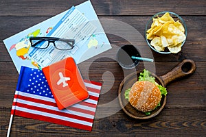 Burger, chips, map, tickets and usa flag for gastronomical tourism to America on wooden background top view