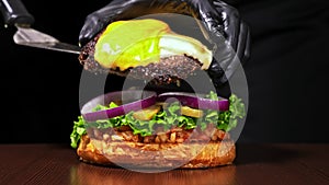 Burger is cooking on black background in black food gloves. Very luscious air bun and marbled beef. Restaurant where