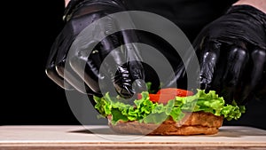 Burger is cooking on black background in black food gloves. Very luscious air bun and marbled beef. Restaurant where