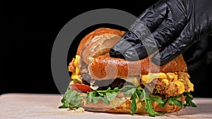 Burger is cooking on black background in black food gloves. Very luscious air bun and marbled beef. Restaurant where