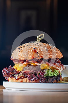 Burger with a cutlet of marbled beef with cheddar cheese, slices of bacon, tomato and pickle in a white bun with sesame