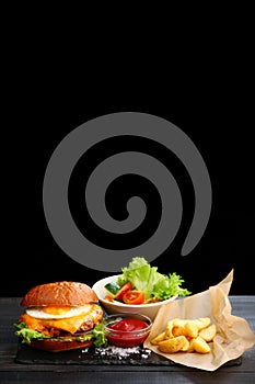 Burger with egg with fries and ketchup sauce on wooden table and black background. tasty cheesburger