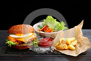 Burger with egg with fries and ketchup sauce on wooden table and black background. tasty cheesburger