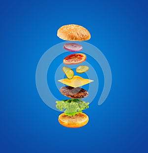 Burger with flying ingredients on blue background. Delicious hamburger in the air.