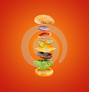 Burger with flying ingredients on orange background. Delicious hamburger in the air.